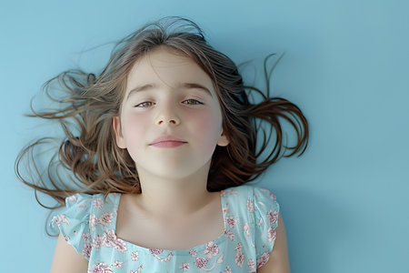 Portrait of a nice young girl with her arms thrown back, causing her hair to fly, wearing a top and isolated on a blue background. The scene captures a vibrant and joyful moment. AI generated.の素材