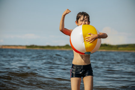 Little boy playing with a beach ball in the water on a sunny dayの写真素材