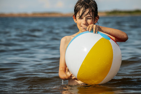 Cute little boy playing with a ball in the sea on a hot summer dayの写真素材