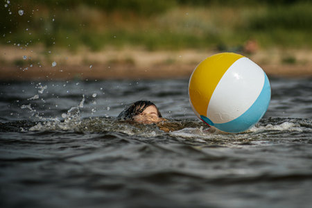 Young woman swimming with a beach ball in the water of a lakeの写真素材