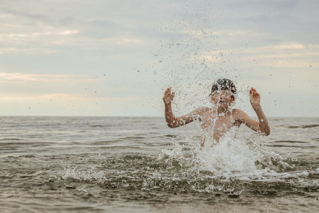 Boy splashing water on the beach at sunset. Cute boy having fun on the sea.の写真素材