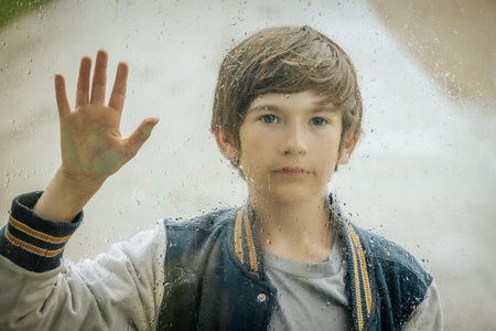 Portrait of a boy looking through a window with raindrops.