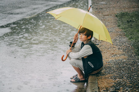 Little boy with yellow umbrella in the rain on a rainy day.の写真素材