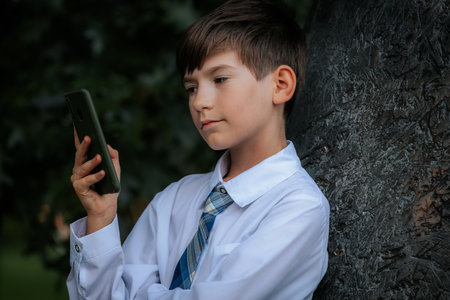 Portrait of a boy in a white shirt and tie with a smartphone in his hands.の写真素材