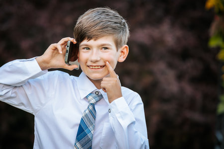 Cute schoolboy in shirt and tie talking on mobile phone outdoorsの写真素材