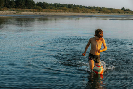 Young boy playing with a ball in the water of the river.の写真素材