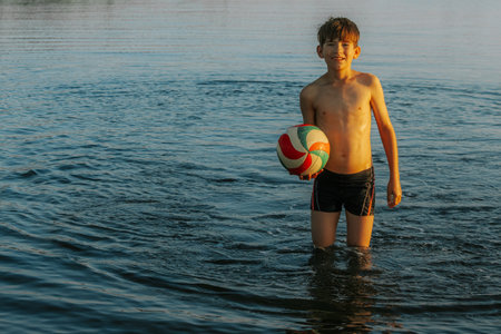 boy playing with a ball in the water on the beach in summerの写真素材