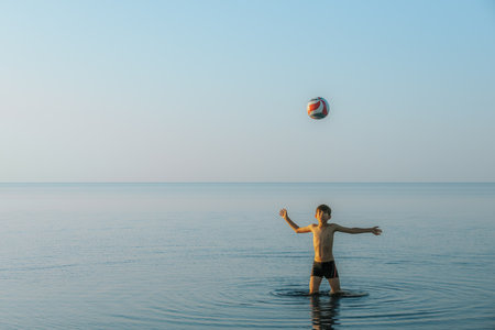 Young man playing with a ball in the sea on a sunny dayの写真素材
