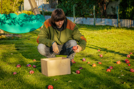 A young man in a green jacket cuts an apple in the gardenの写真素材