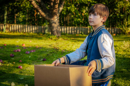 A boy in a school uniform sits on the grass and holds a box in his hands.の写真素材