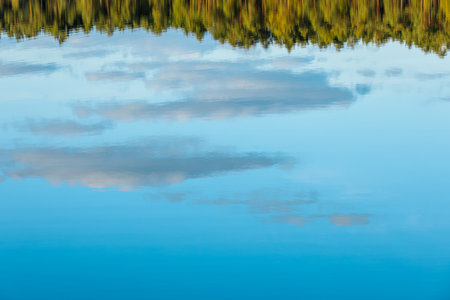 Reflection of trees and clouds in the calm water of a lakeの写真素材
