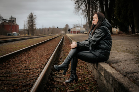 Young beautiful brunette girl in a black jacket and jeans posing on the railroad.