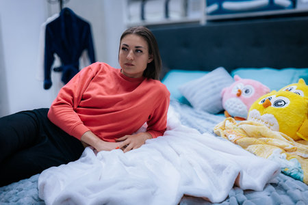 sad young woman sitting on bed and looking at camera at homeの写真素材
