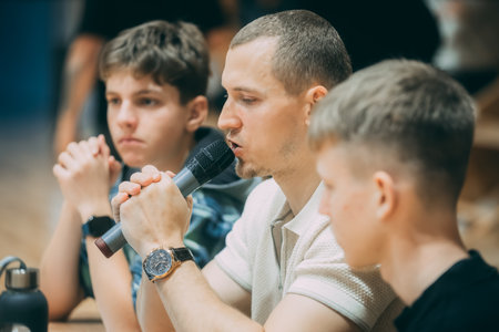 Young man singing into a microphone while his friends sitting on the floorのeditorial素材