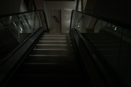 Downward escalator in a contemporary setting, featuring glass railings and soft lighting, highlighting modern architecture and providing ample copy space for design purposesの写真素材