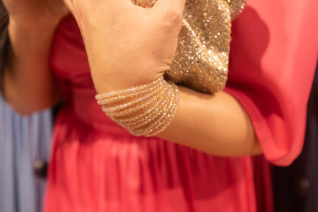 Stylish female figure in pink dress, adorned with sparkling bracelet and clutch purse, highlights...