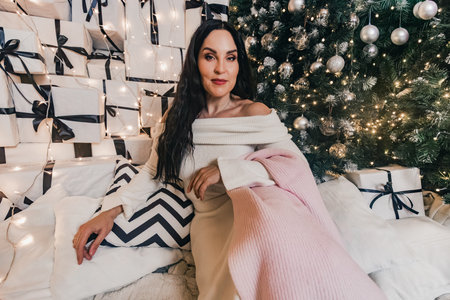 Stylish female figure in white sweater, surrounded by wrapped gifts and a beautifully lit Christmas...