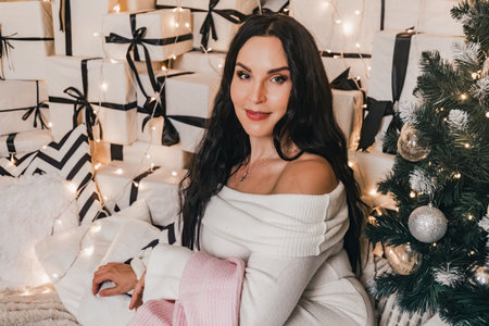 Female figure in white sweater surrounded by wrapped gifts and soft lights, evoking a cozy holiday ambiance, perfect for seasonal themes and celebrationsの写真素材