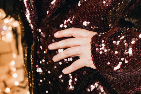 Hand elegantly placed on a sparkling sequined outfit, highlighting the rich textures and colors, with a blurred background of twinkling lights enhancing the festive moodの写真素材