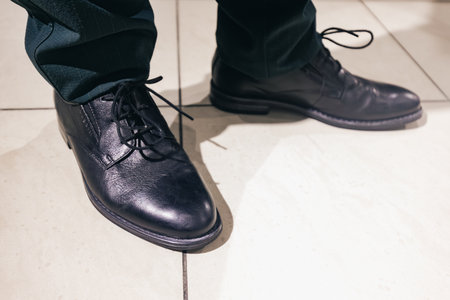 Black leather dress shoes are prominently displayed on a tiled floor, highlighting a blend of...