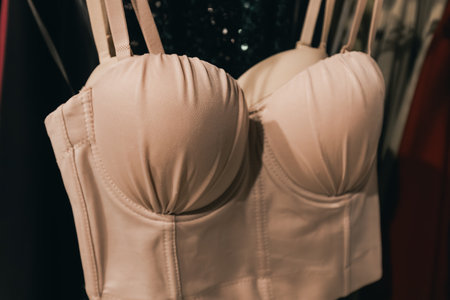 Stylish beige corset featuring structured cups and straps, elegantly displayed on a hanger, highlighting fashion design and textile quality in a retail settingの写真素材