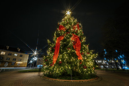 Festive Christmas tree decorated with glowing lights and red ribbons, illuminated in a square at night, enhancing the joyful holiday spirit and ambianceのeditorial素材