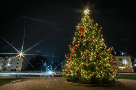 Beautifully decorated Christmas tree with sparkling lights and red ornaments, situated in a circular plaza at night, enhancing the holiday spirit and ambianceのeditorial素材