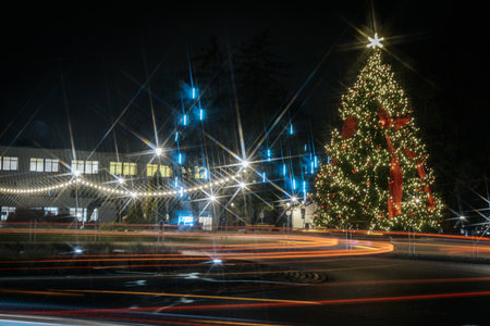 Festive Christmas tree illuminated with lights and ribbons, surrounded by decorations, creating a warm holiday ambiance at night, showcasing seasonal joy and celebrationの写真素材