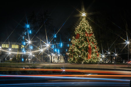 Beautifully lit Christmas tree with vibrant decorations stands in a festive setting, illuminated by street lamps and colorful light trails, evoking holiday cheerの写真素材