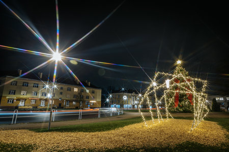 Brightly lit Christmas tree with decorations stands in a festive setting, illuminated by street lamps, creating a warm winter ambiance with copy spaceのeditorial素材