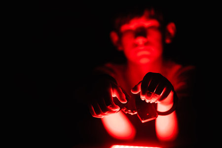 Child with hands extended in darkness, surrounded by vibrant red light, creating an engaging scene that emphasizes creativity and playful explorationの写真素材