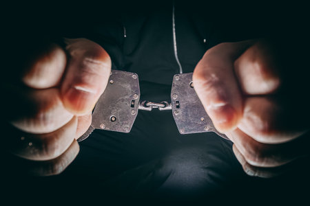 Close-up of hands pulling apart metal handcuffs, symbolizing the desire for freedom, with a dark atmosphere enhancing the dramatic tension and emotional impact of the sceneの写真素材
