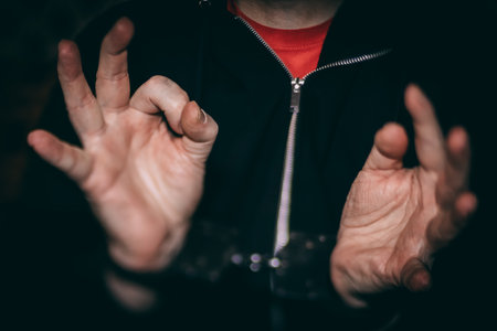 Person in black hoodie is using hands to express gestures, emphasizing communication and body language in a low-light setting, creating an engaging atmosphereの写真素材