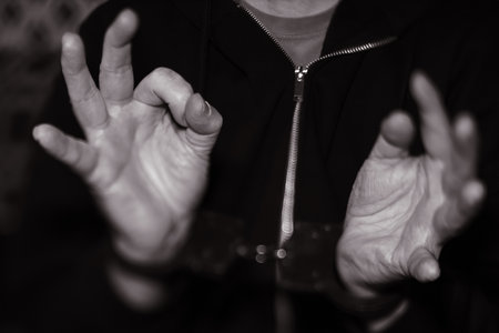 Person's hands in black hoodie, displaying different gestures, emphasizing expressive communication and body language in a striking monochrome environmentの写真素材
