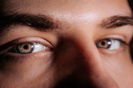Close-up view of young man's eyes, highlighting unique iris patterns and eyelashes, illuminated...