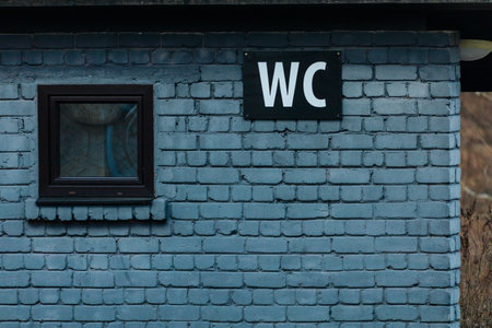 Outdoor restroom structure features a blue brick wall, small window, and a clear WC sign, highlighting its rustic charm and functional designの写真素材