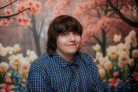Male subject with dark hair smiles in front of a colorful floral backdrop, featuring blooming...