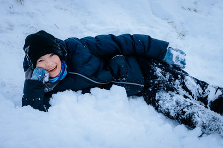 Happy child in winter clothing, enjoying snow play while lying on the ground, surrounded by fluffy white snow, capturing the essence of winter joy and outdoor funの写真素材