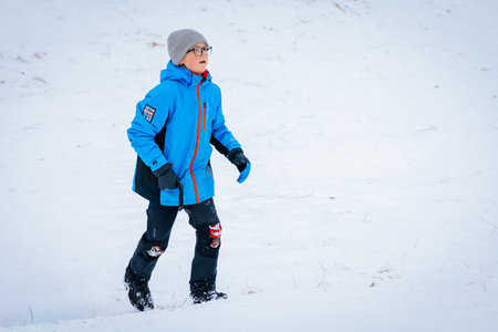 Valmiera, Latvia - January 02, 2026: Boy in blue winter jacket walks through snow-covered landscape, enjoying the beauty of winter outdoorsのeditorial素材