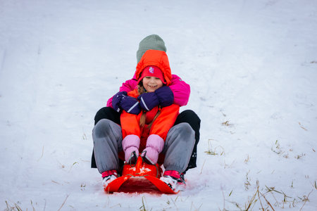 Valmiera, Latvia - January 02, 2026: Two girls are sledding down snowy hill, wearing colorful winter...