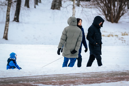 Valmiera, Latvia - January 02, 2026: Family members walking in snowy park, child playing in snow,...