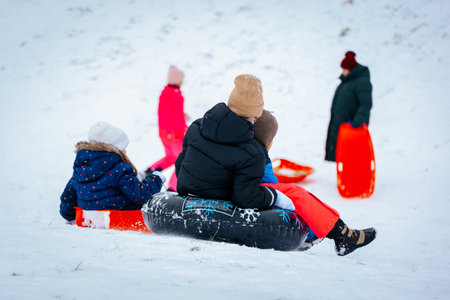 Valmiera, Latvia - January 02, 2026: Children are sledding down snowy hill, wearing colorful winter clothing, creating a joyful atmosphere in the winter landscapeのeditorial素材