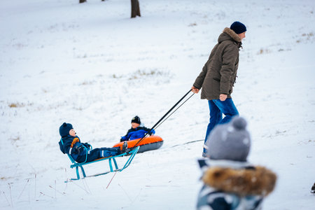 Valmiera, Latvia - January 02, 2026: A father enjoys winter with his kids, pulling them on sleds through the snow-covered landscape, creating joyful memoriesのeditorial素材