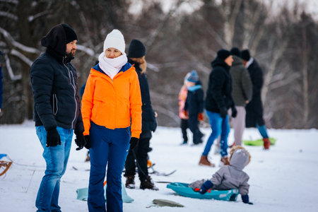 Valmiera, Latvia - January 02, 2026: Woman in orange jacket stands with man on snowy hill, families...