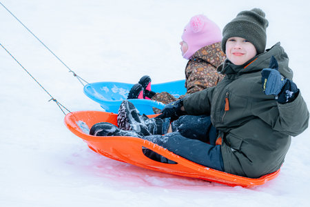 Valmiera, Latvia - January 11, 2026: Young boy and girl are playing on bright sleds in the snow,...