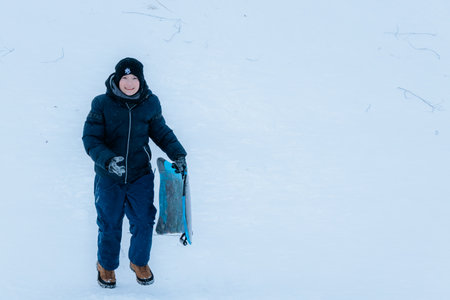 Valmiera, Latvia - January 11, 2026: Young boy is happily holding sled in snowy environment, dressed...