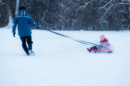 Valmiera, Latvia - January 11, 2026: Man is pulling a little girl on a sled across a snowy field, capturing the joy of winter activities and family momentsのeditorial素材