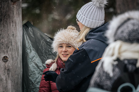 Ligatne, Latvia - January 11, 2026: Smiling woman wearing a furry hat engages in conversation with a friend in a snowy forest settingのeditorial素材