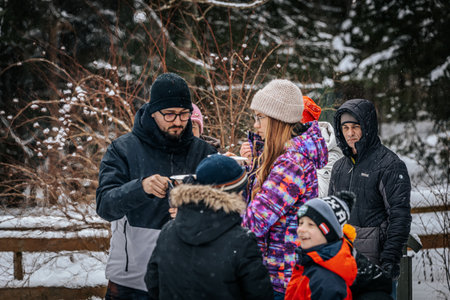 Ligatne, Latvia - January 11, 2026: Friends are gathered in snowy forest, sharing hot drinks while wearing warm winter clothing, creating a joyful ambianceのeditorial素材