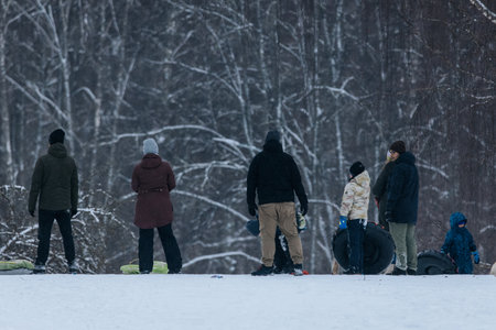 Valmiera, Latvia - January 11, 2026: Diverse group of people in winter attire, standing on snowy hill, ready for sledding and tubing in tranquil snowy environmentのeditorial素材